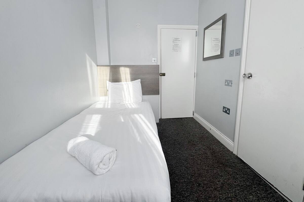 A hotel room with a bed, a folded towel, a door, and a mirror on the wall.