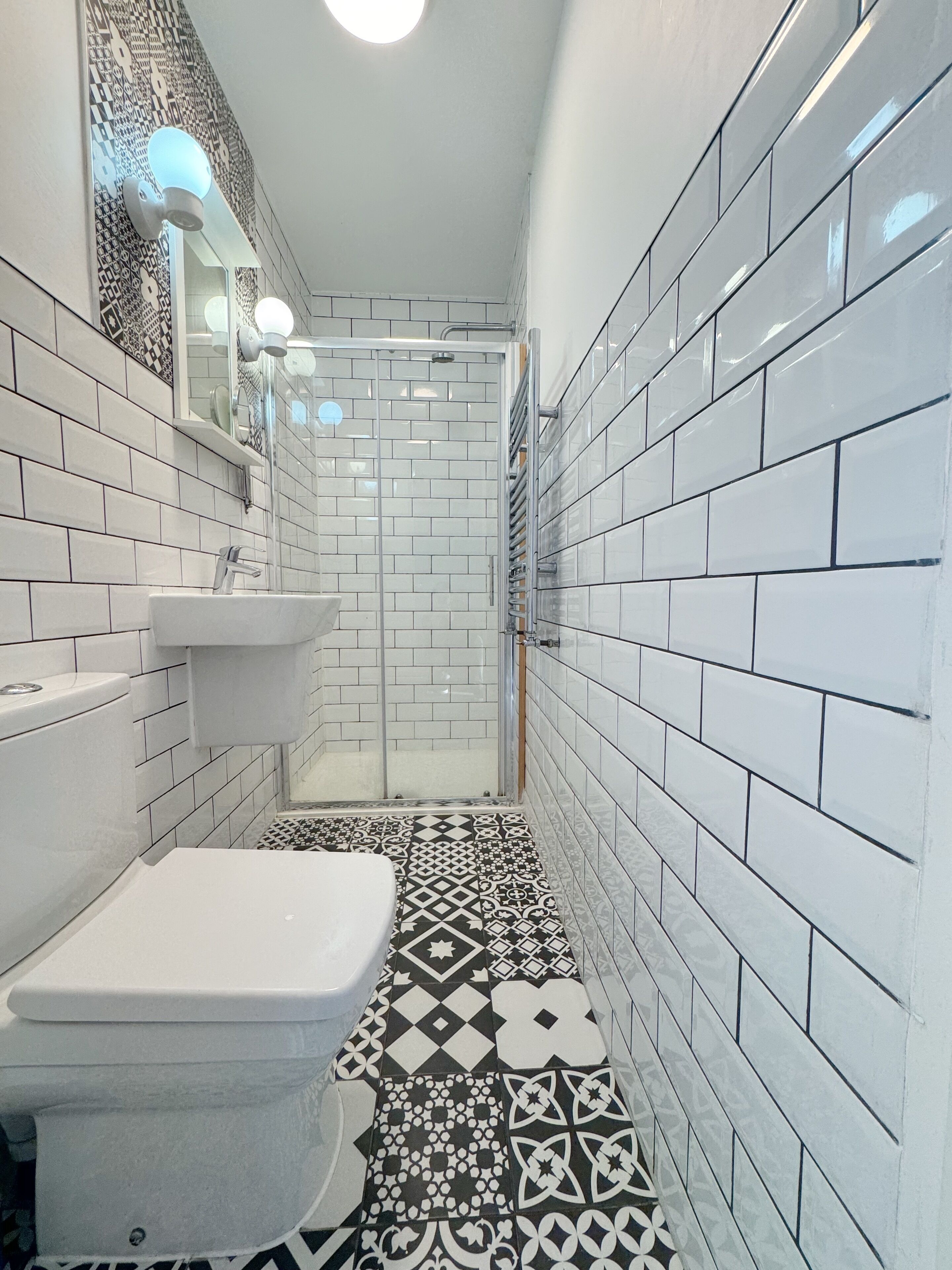 A bathroom with white tiles, a sink, a toilet, and a shower area.