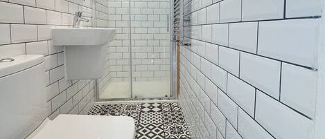 A bathroom with white tiles, a sink, a toilet, and a shower area.