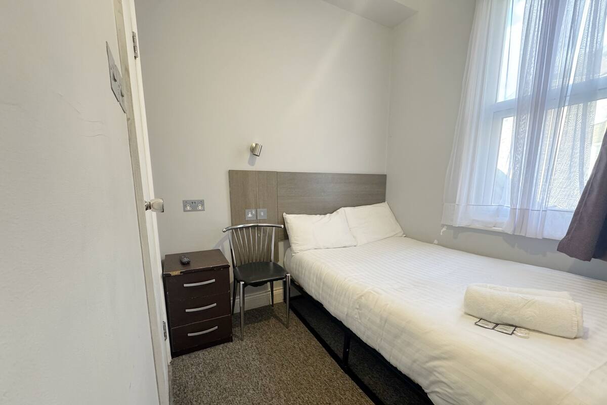 A hotel room with a bed, a chair, a nightstand, and a window with curtains.