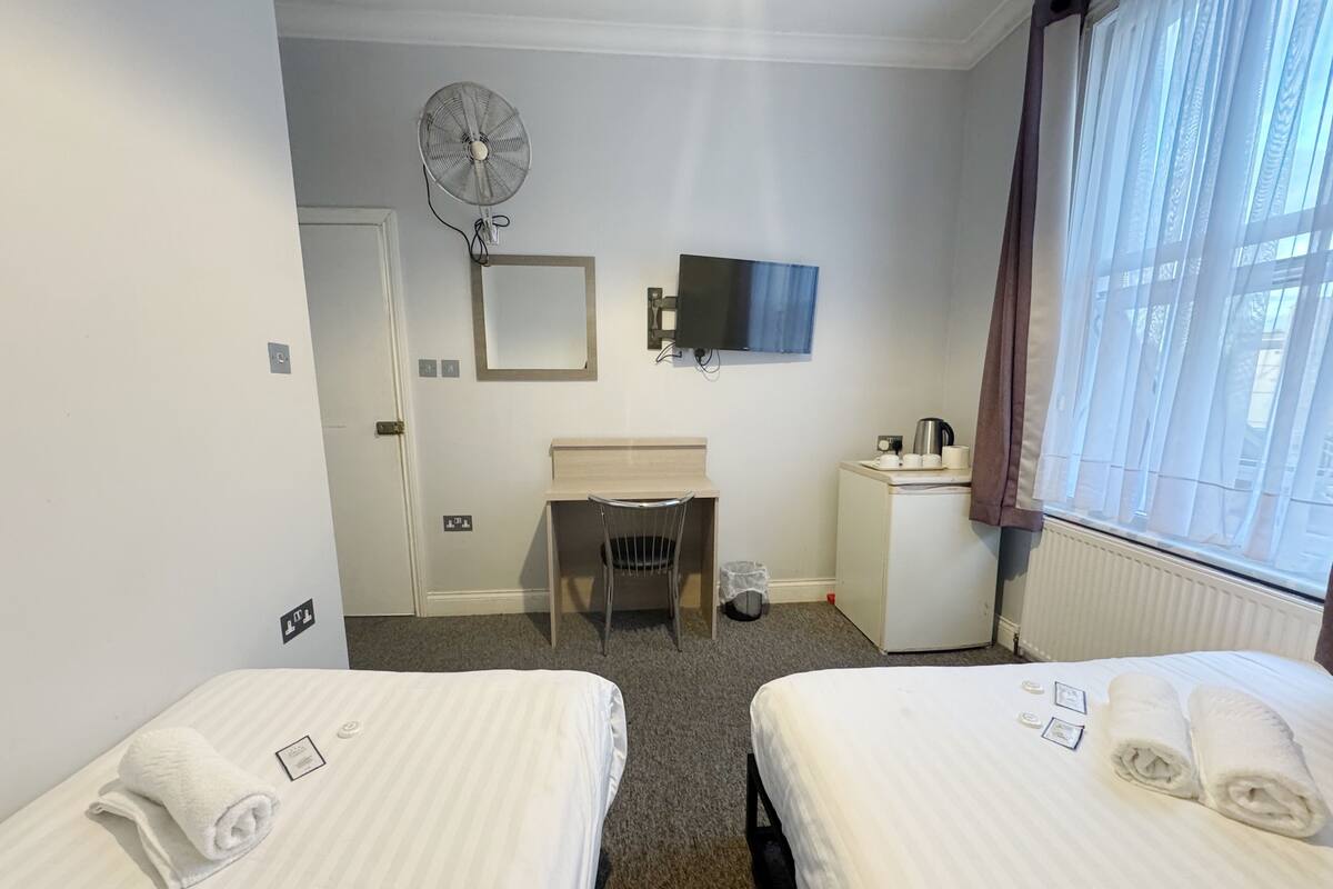 A hotel room with two beds, a desk, a chair, a TV, and a window with curtains.