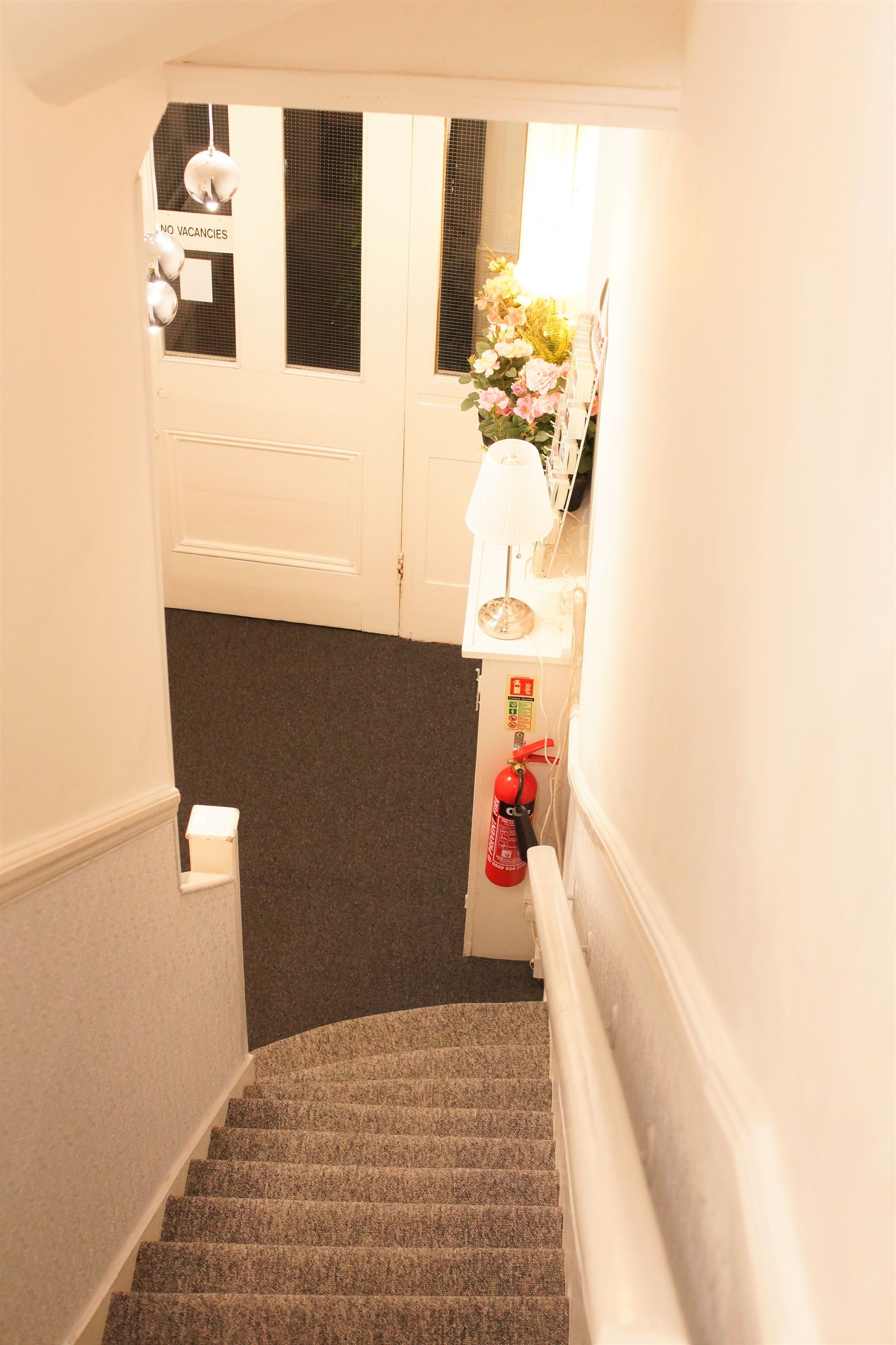 Un escalier dont les marches sont recouvertes de moquette, un extincteur et une pancarte « COMPLET » sur une porte.