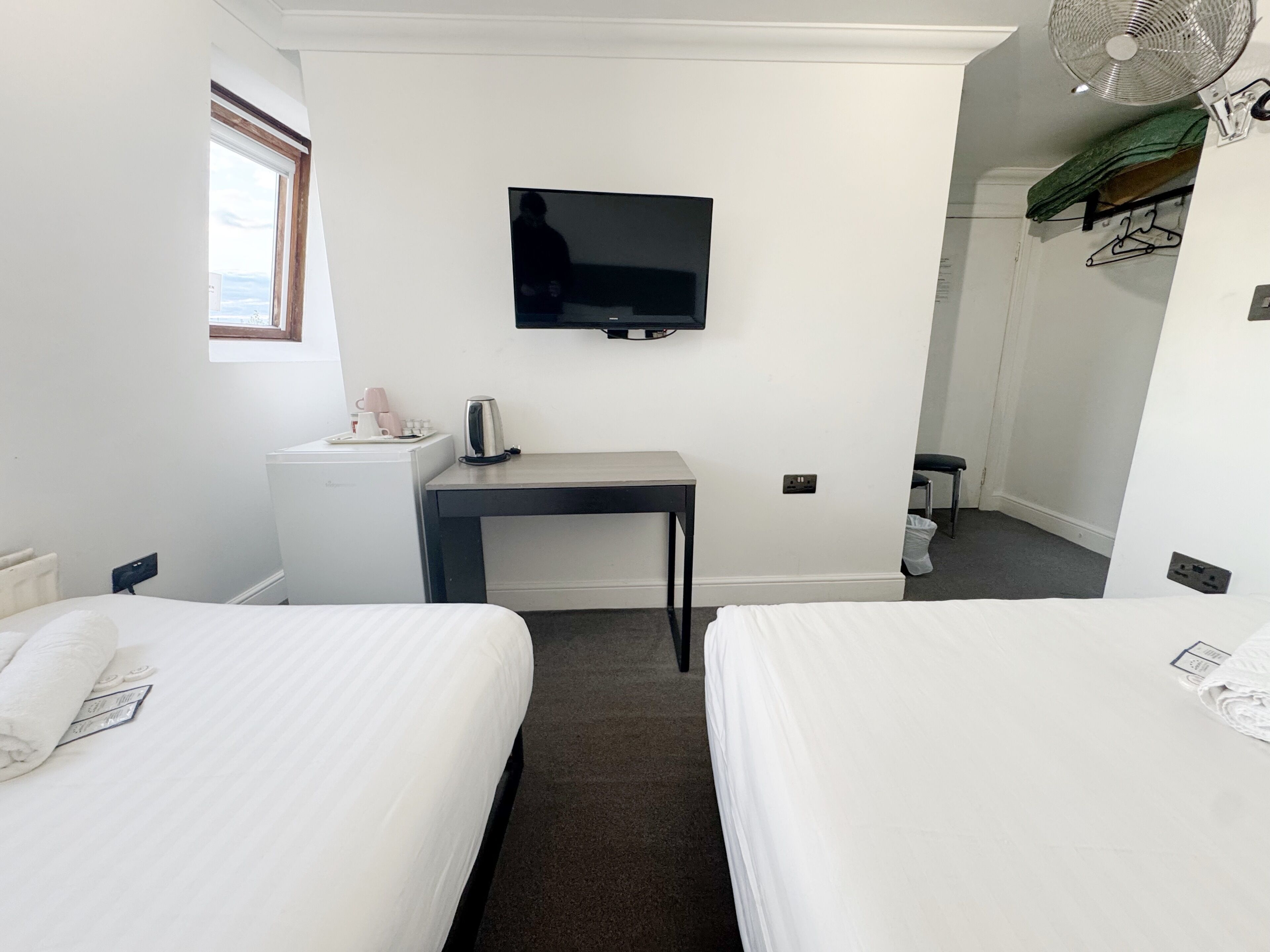 Een hotelkamer met twee bedden, een bureau, een televisie, een waterkoker en een raam.