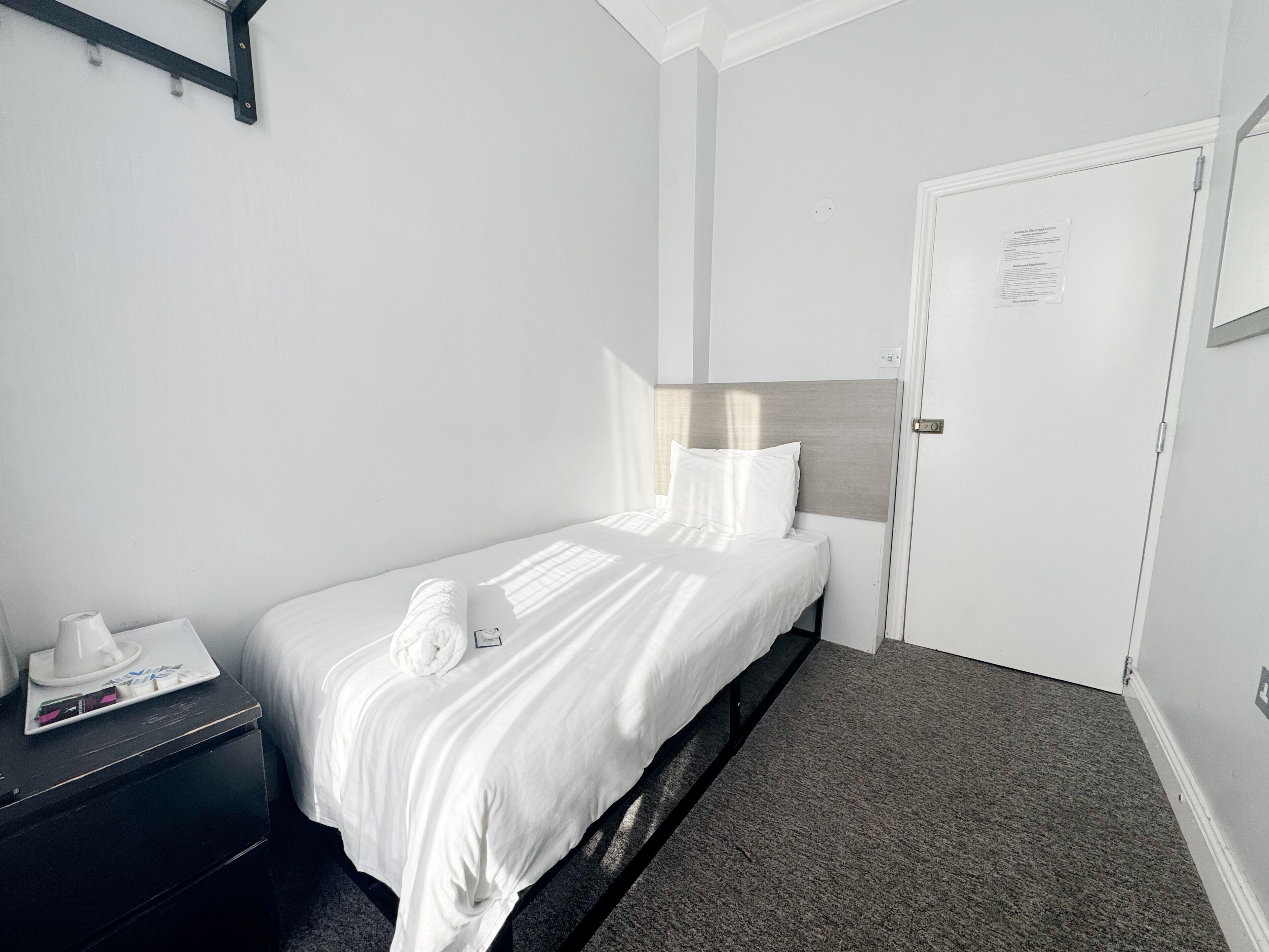 Een hotelkamer met een enkel bed, een nachtkastje, een deur en een wandplank.