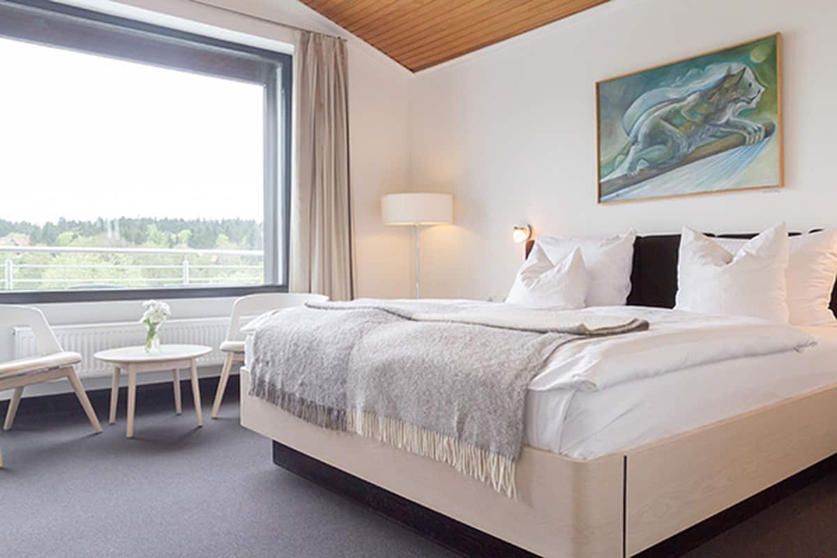 A bedroom with a large bed, a bedside table, a chair, a lamp, and a painting on the wall.