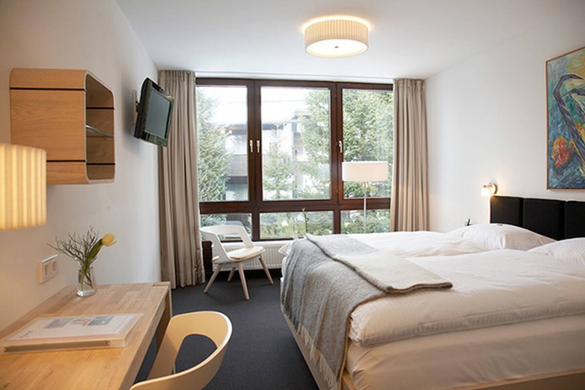 A hotel room with a bed, a desk, a chair, a TV, and a window with curtains.