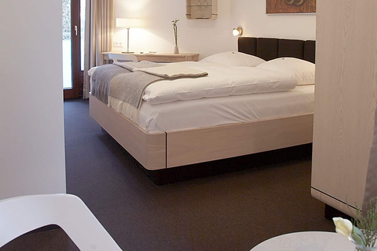 A hotel room with a bed, bedside table, lamp, and a painting on the wall.
