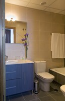 Ein Badezimmer mit Waschbecken, Toilette und Badewanne. Ein Mülleimer und ein Spiegel befinden sich über dem Waschbecken.