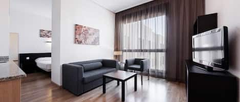 Ein modernes Hotelzimmer mit Sofa, Sessel, Couchtisch und Flachbildfernseher.