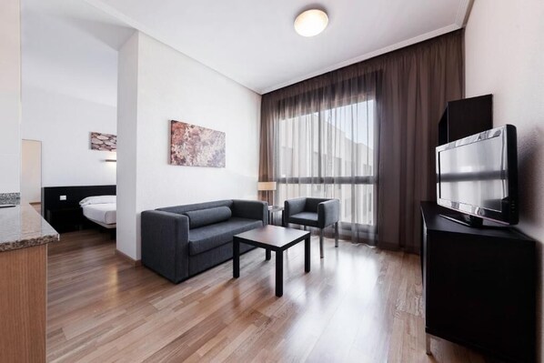 Una habitación de hotel moderna con sofá, sillón, mesa de centro y televisor de pantalla plana.