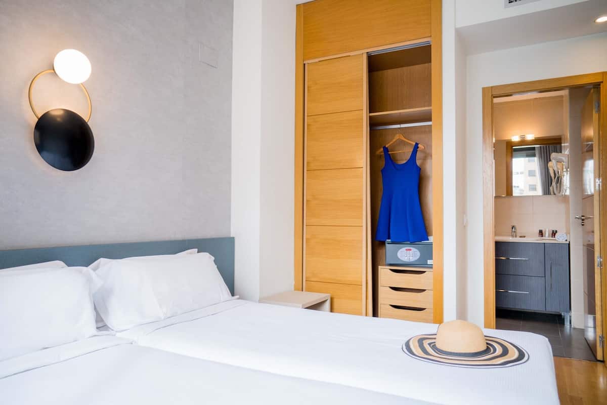 A hotel room with a bed, a wardrobe, a bathroom, and a wall-mounted light fixture.