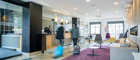 Eine moderne Hotelhalle mit Empfangstresen, Sitzgelegenheiten und großen Fenstern.