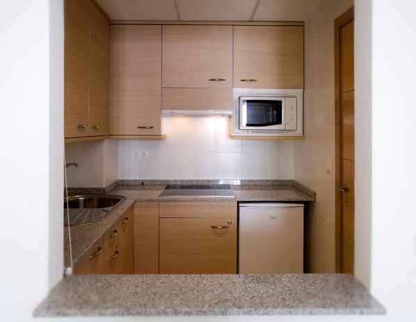 Una cocina compacta con armarios de madera, microondas integrado, pileta y lavavajillas.