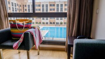 A room with a view of a swimming pool, a striped bag on a chair, and a table with a phone.