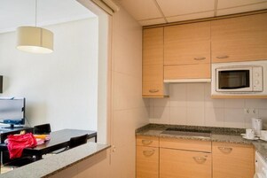 A compact kitchen with wooden cabinets, a microwave, a granite countertop, and a dining area with a table and chairs.