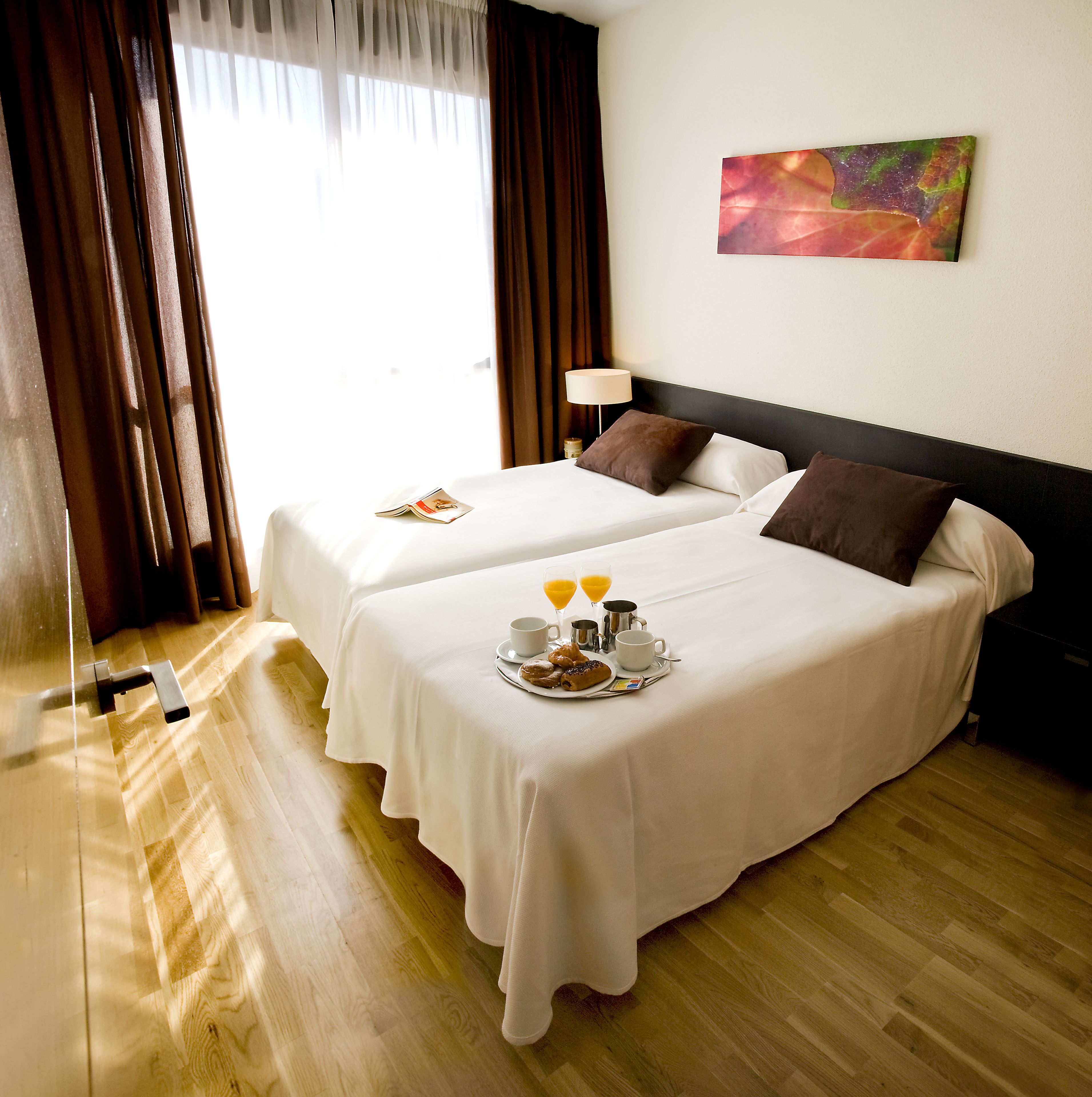 Una habitación de hotel con dos camas, un cuadro en la pared y productos para el desayuno sobre las camas.