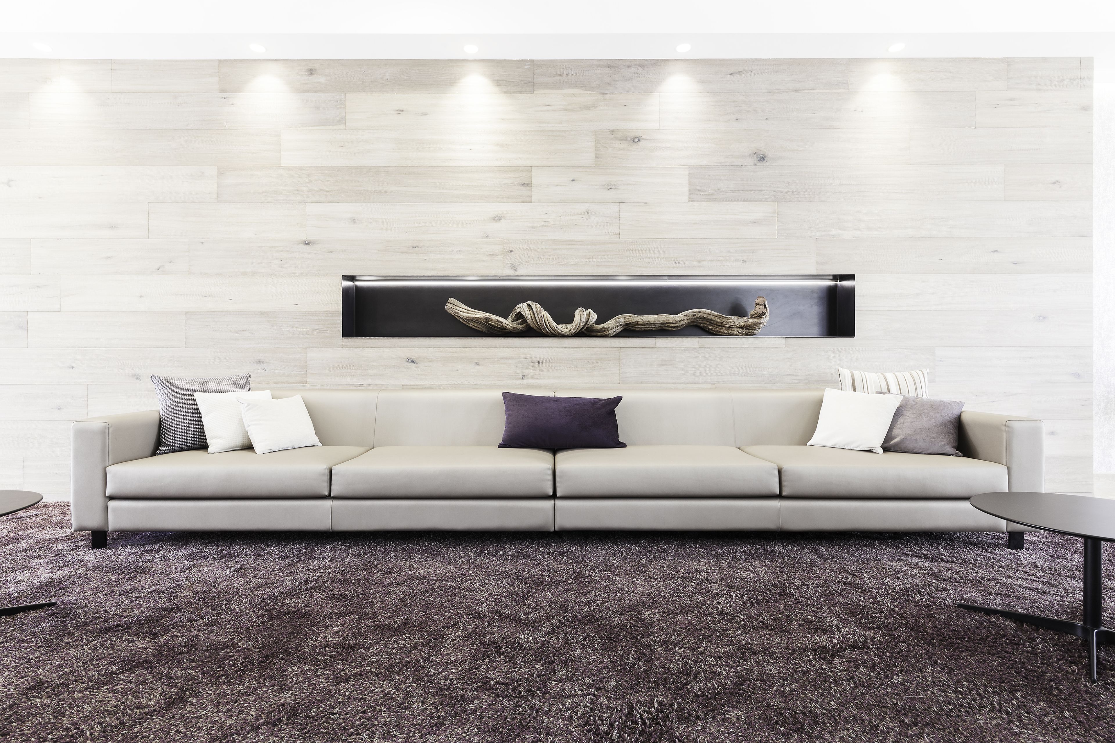 A modern living room with a light-colored sofa, a dark rug, and a minimalist wall art piece.