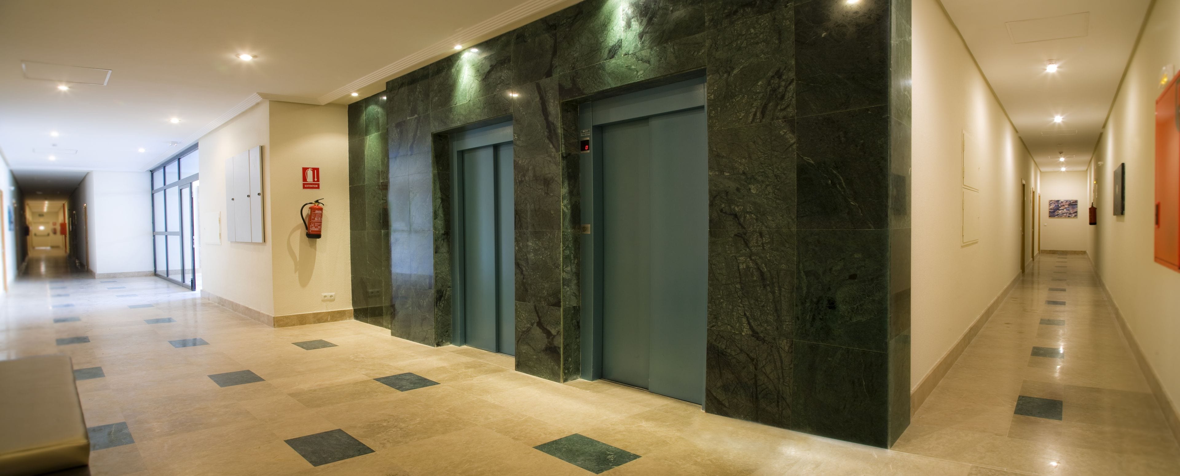 A hallway with two elevators, a fire extinguisher, and a fire alarm.
