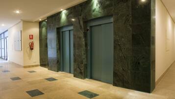 A hallway with two elevators, a fire extinguisher, and a fire alarm.