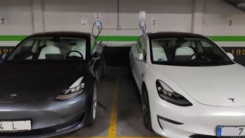 Two Tesla cars parked side by side in a parking garage with green and white walls, and a yellow line marking the parking spaces.