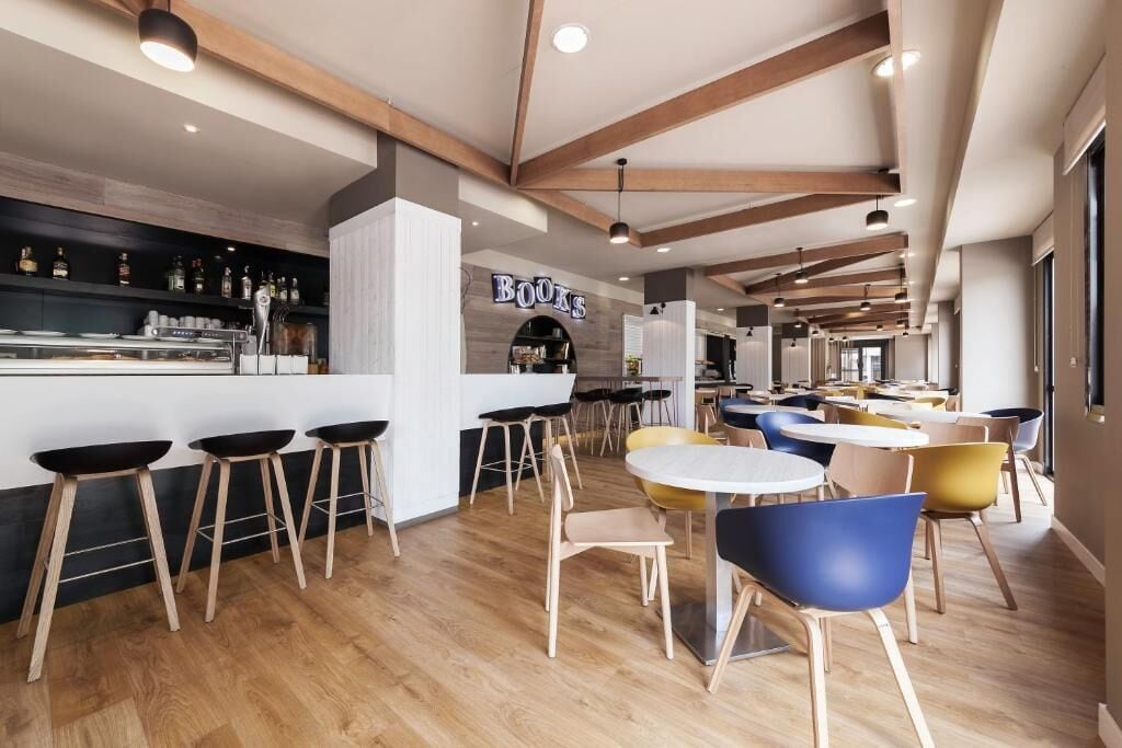 A modern bar area with wooden beams, a bar counter, stools, and tables with chairs.