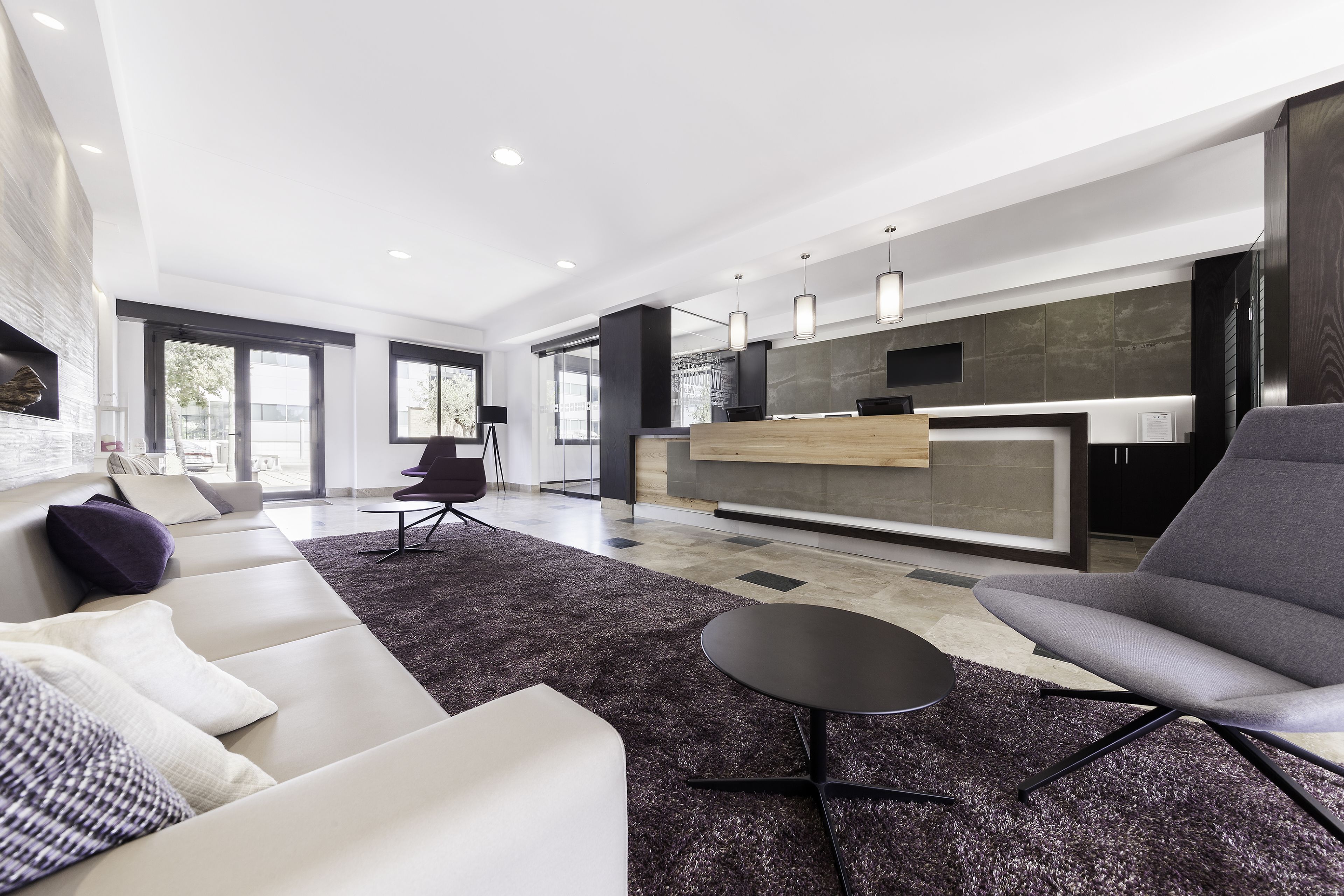 A modern living room with a sofa, a chair, a small table, and a kitchen area with a counter and pendant lights.