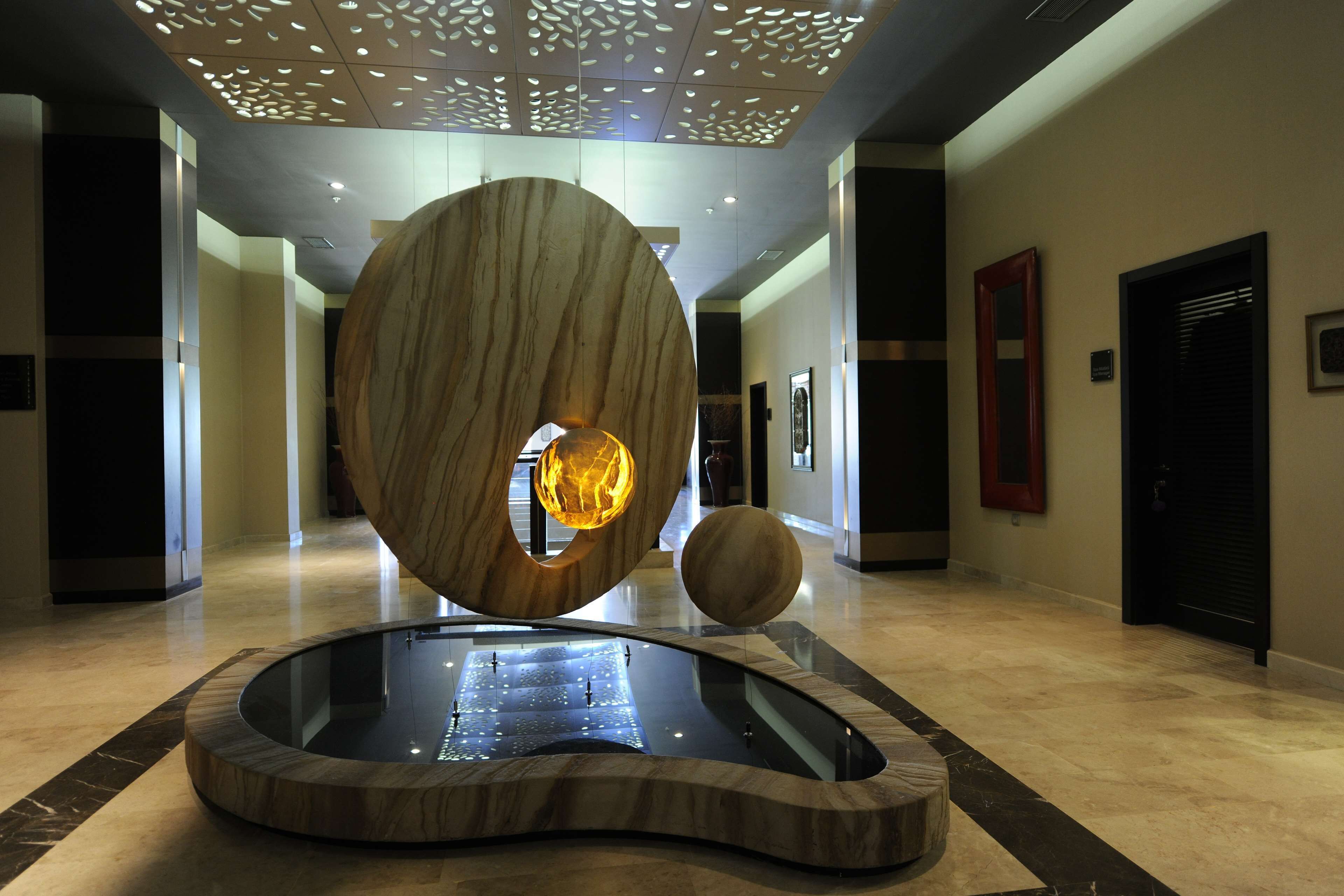 Een moderne lobby met een fontein in het midden, een groot houten sculptuur en een glazen vloer.