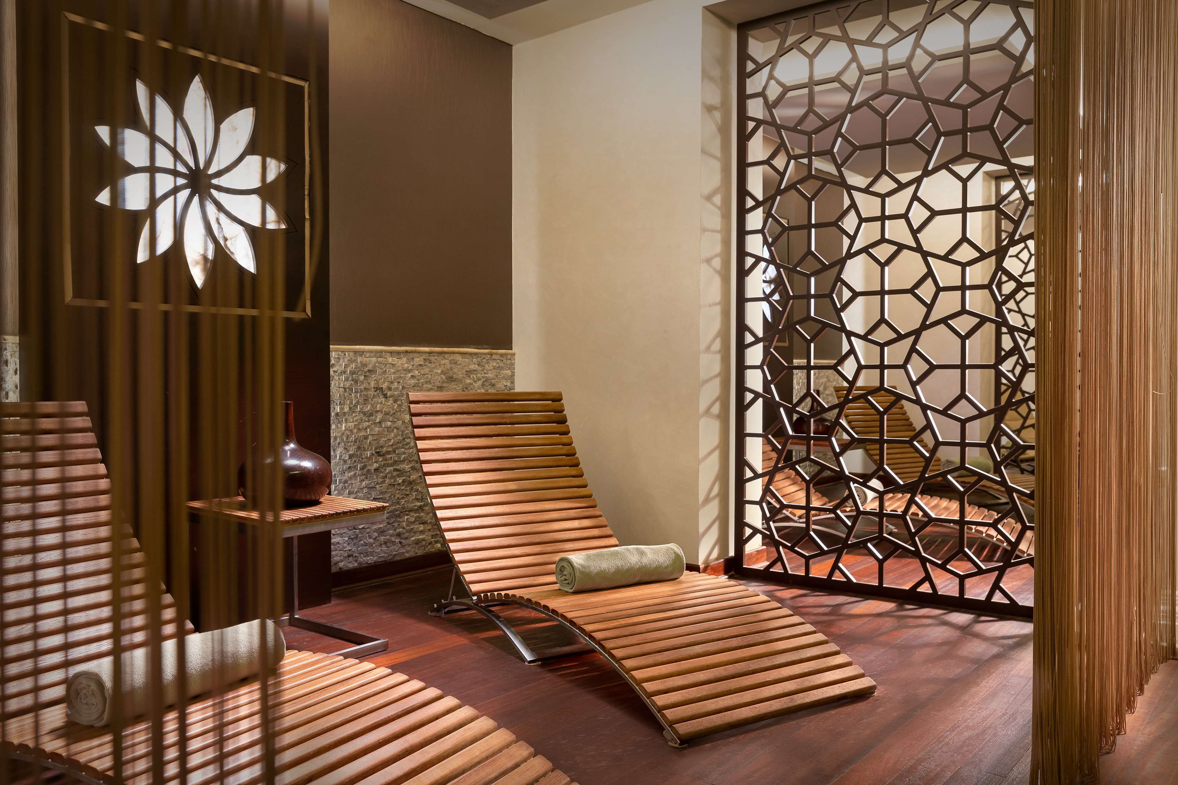 A spa room with wooden loungers, a decorative wall with a geometric pattern, and a large window with a flower design.