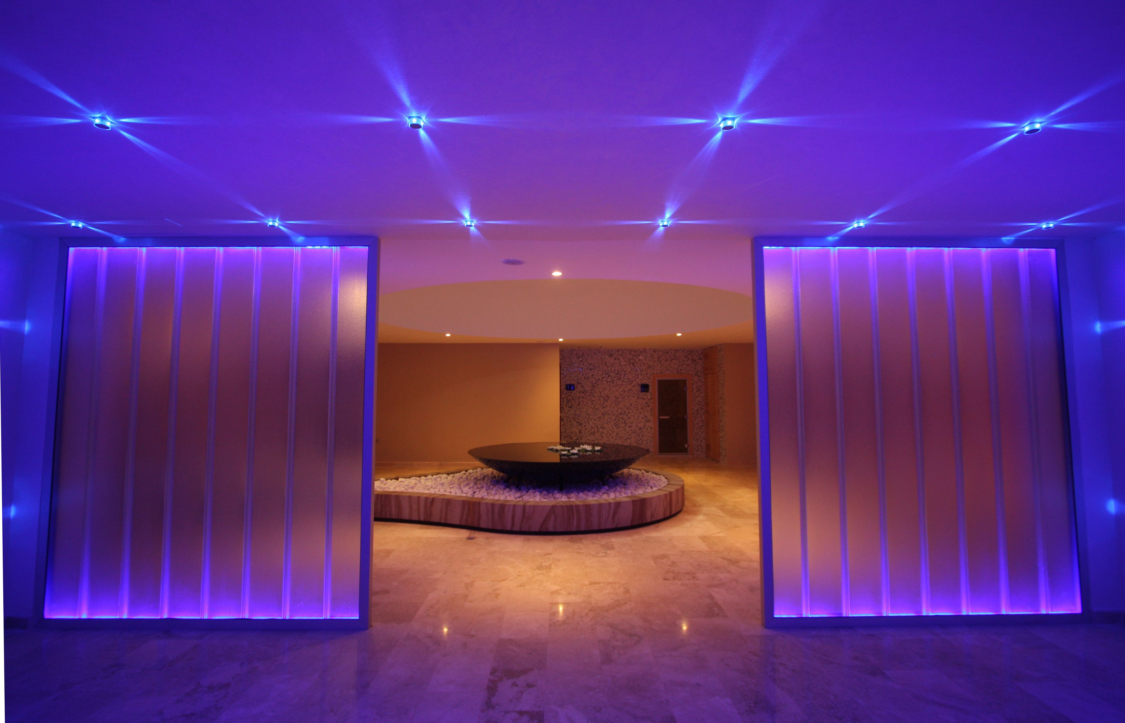 Un espacio de spa moderno con un baño de piedra caliente en el centro, iluminación ambiental y piso de mármol.