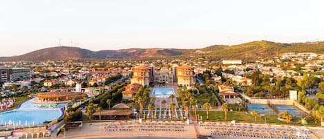 Un resort costero con una gran piscina, zona de playa con tumbonas y un edificio central de varios pisos.