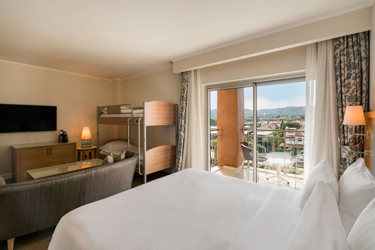 Ein Hotelzimmer mit Bett, Sofa, Schreibtisch, Fernseher und einem Balkon mit Stadtblick.