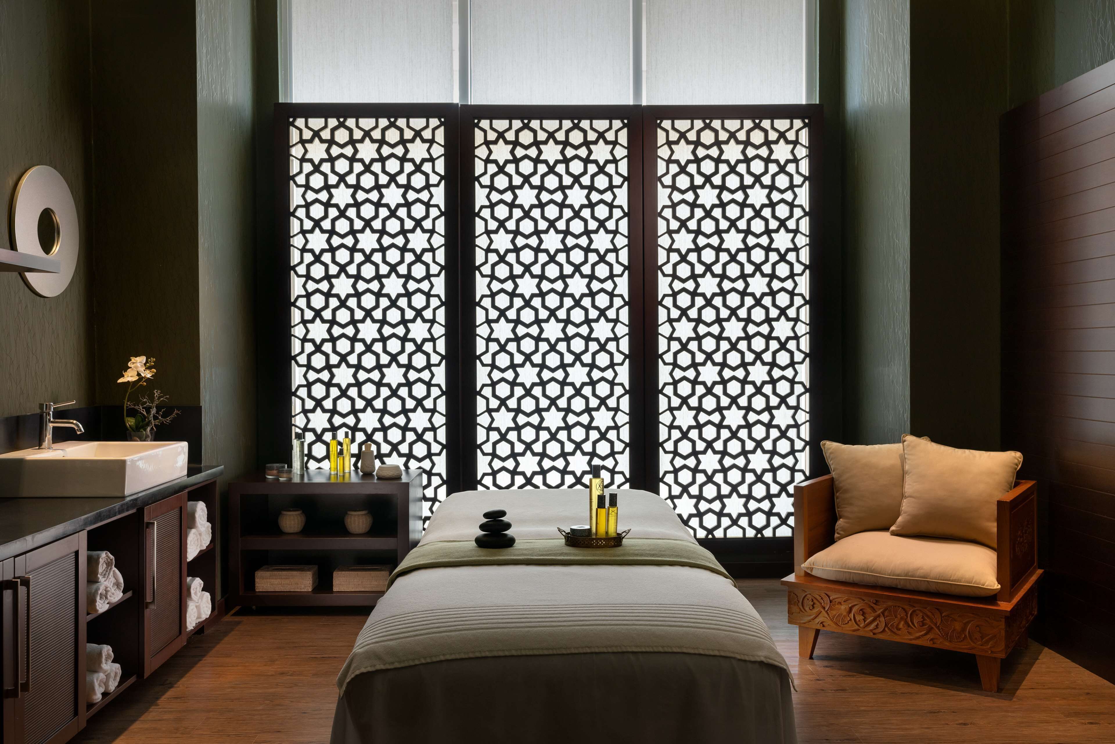 A modern room with a bed, a wooden chair, a small table with candles, and a decorative screen.