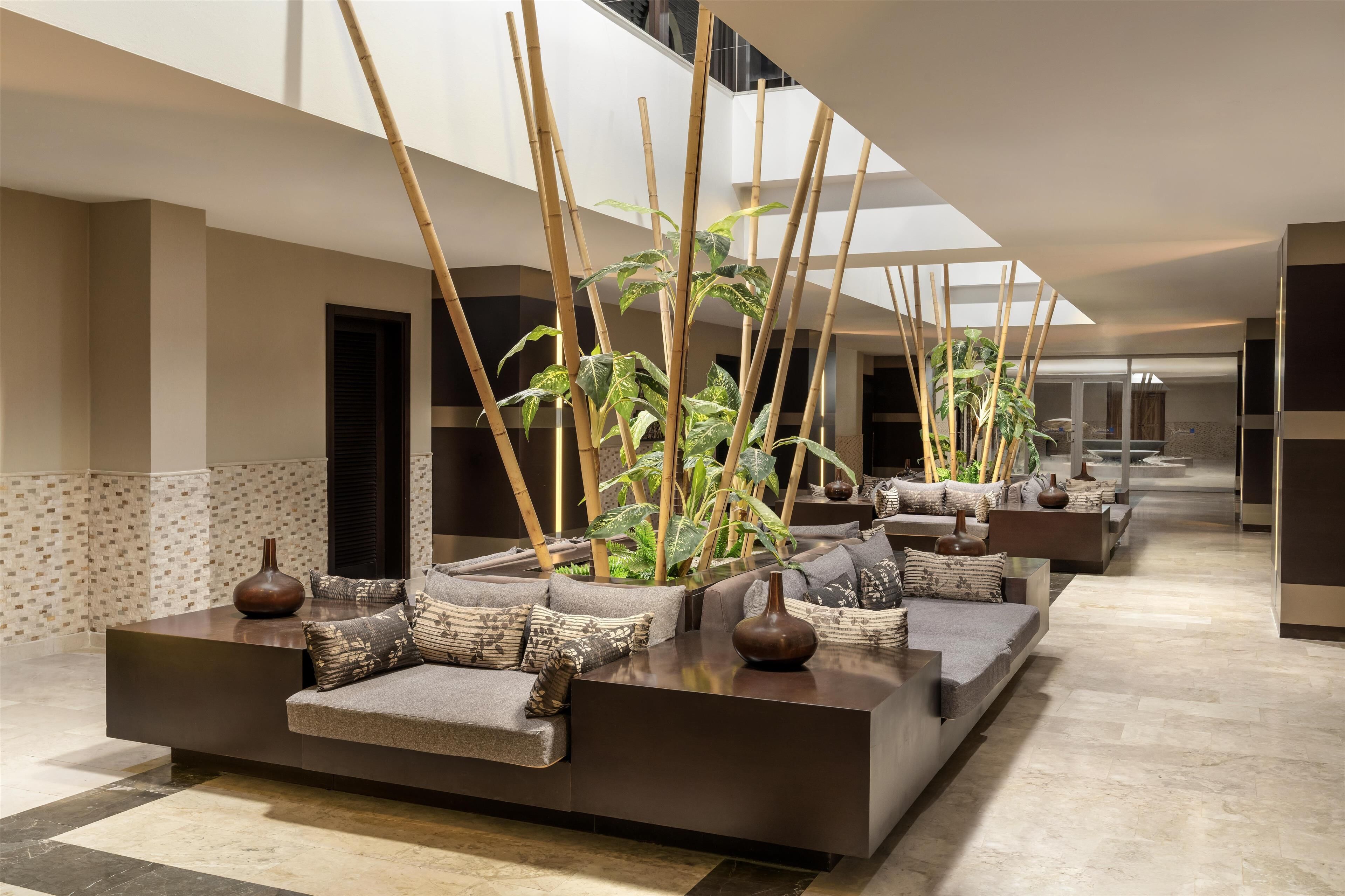Eine moderne Lobby mit einer langen Rezeption, Bambuspflanzen und einer hohen Decke mit Oberlichtern.