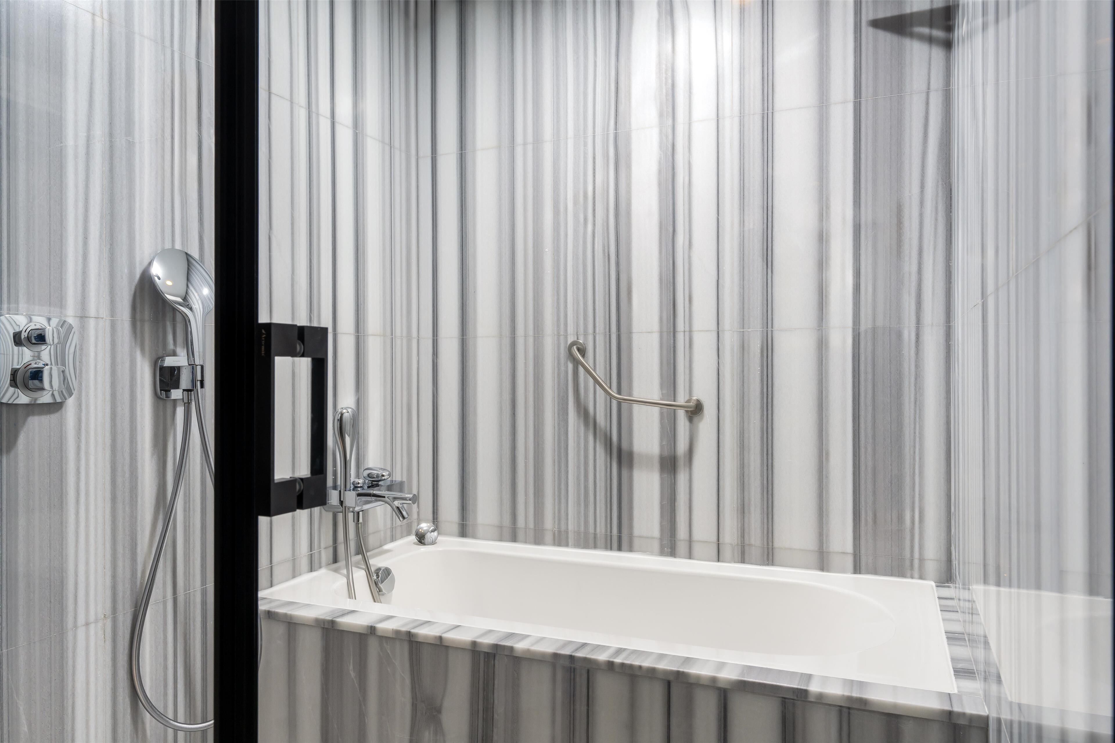 Une salle de bain moderne avec une baignoire blanche, une douchette à main et un robinet mural.