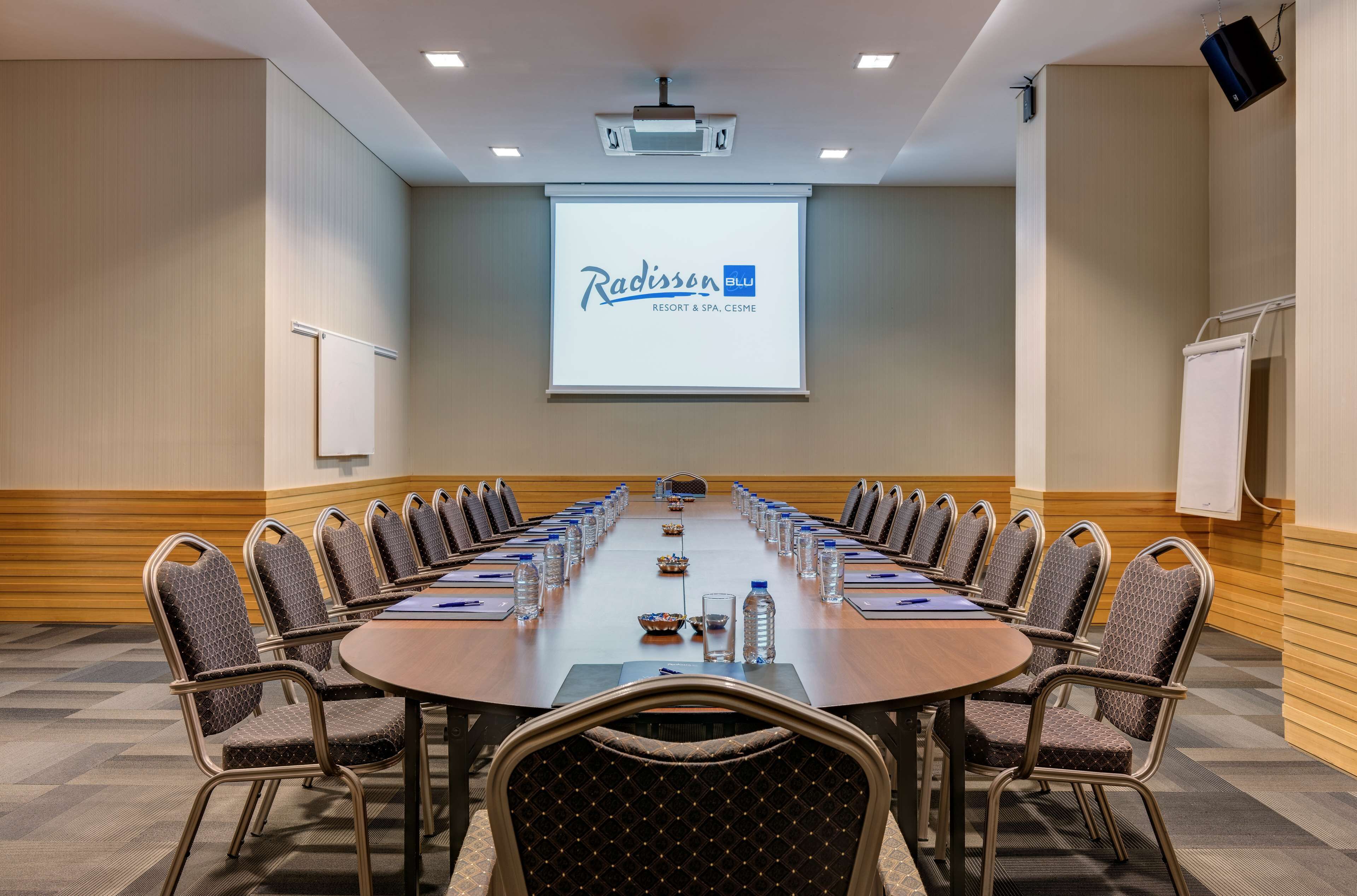 A conference room with a long table, chairs, a projector screen, and a whiteboard.
