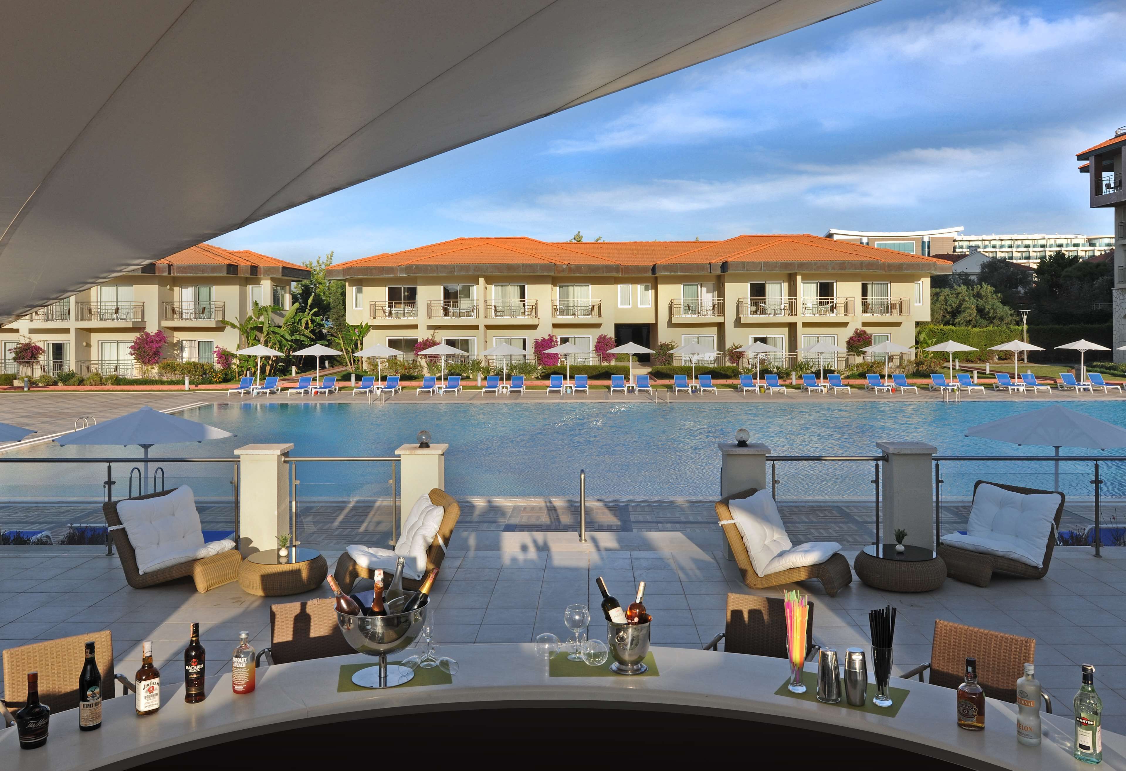 A poolside area with lounge chairs, umbrellas, and a bar with bottles and glasses.