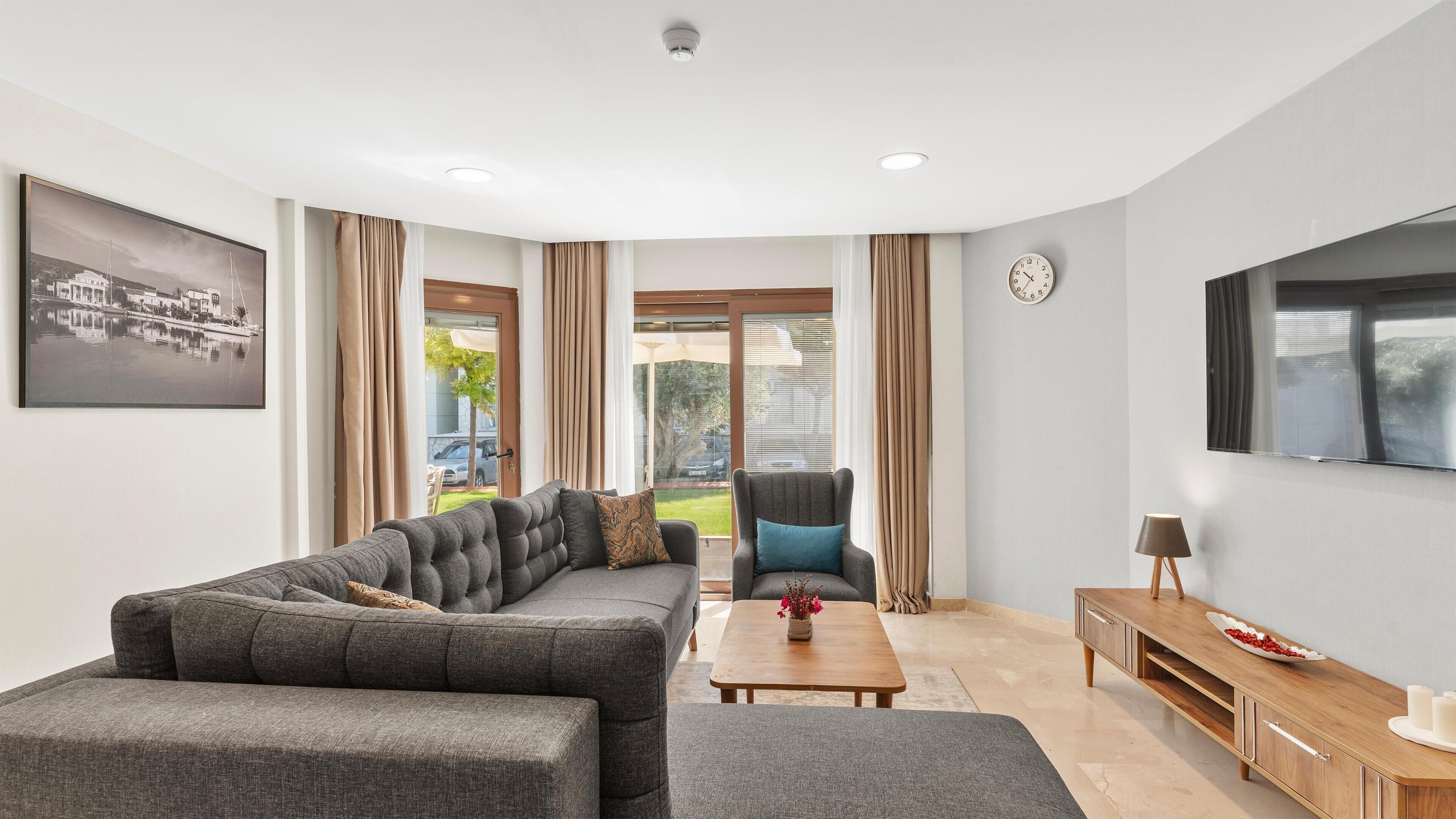 A modern living room with a sofa, armchair, coffee table, TV, and a view of the outdoors.
