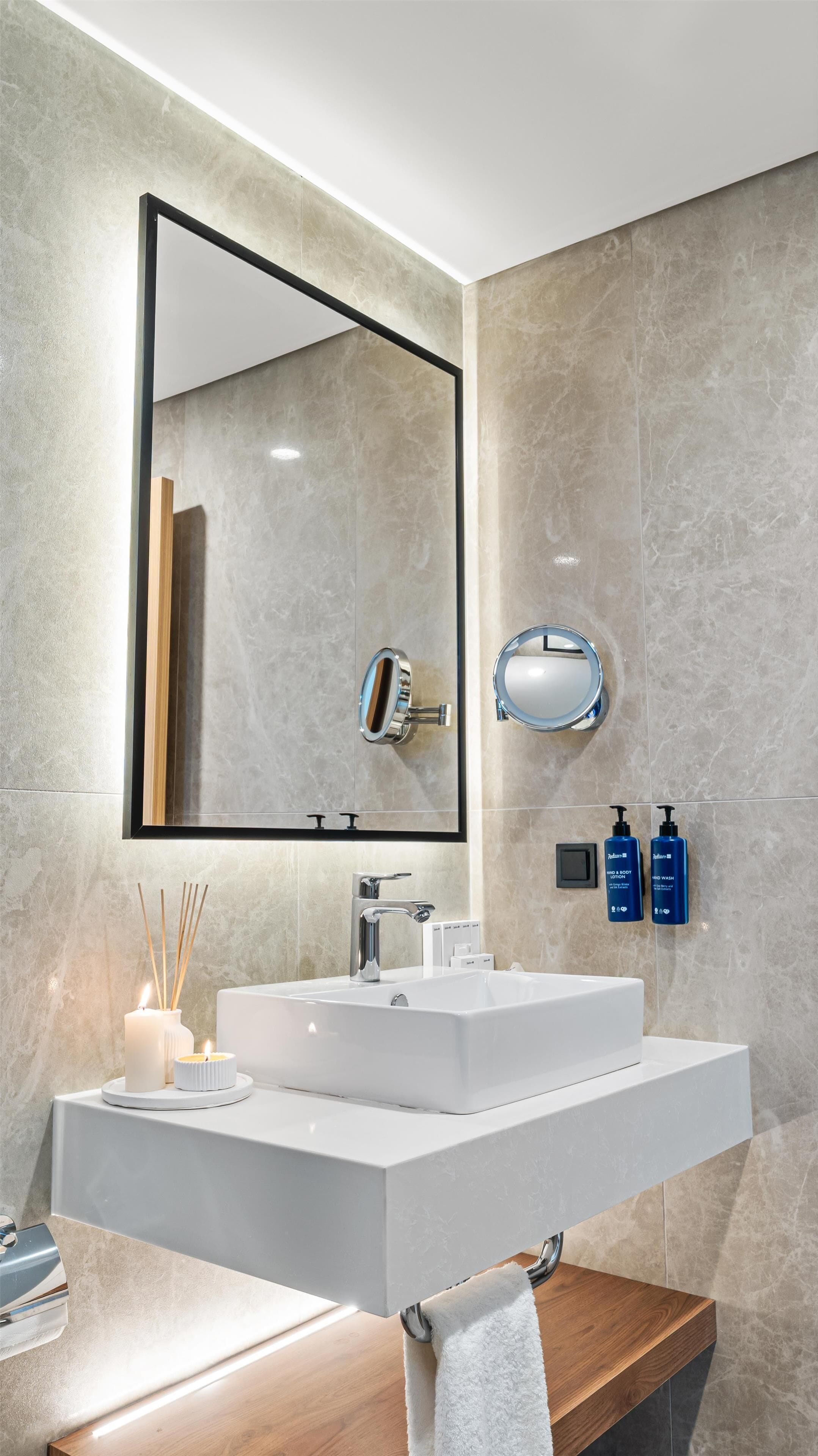 Un baño moderno con un espejo grande, dos lavamanos, un perchero para toallas y artículos de aseo.