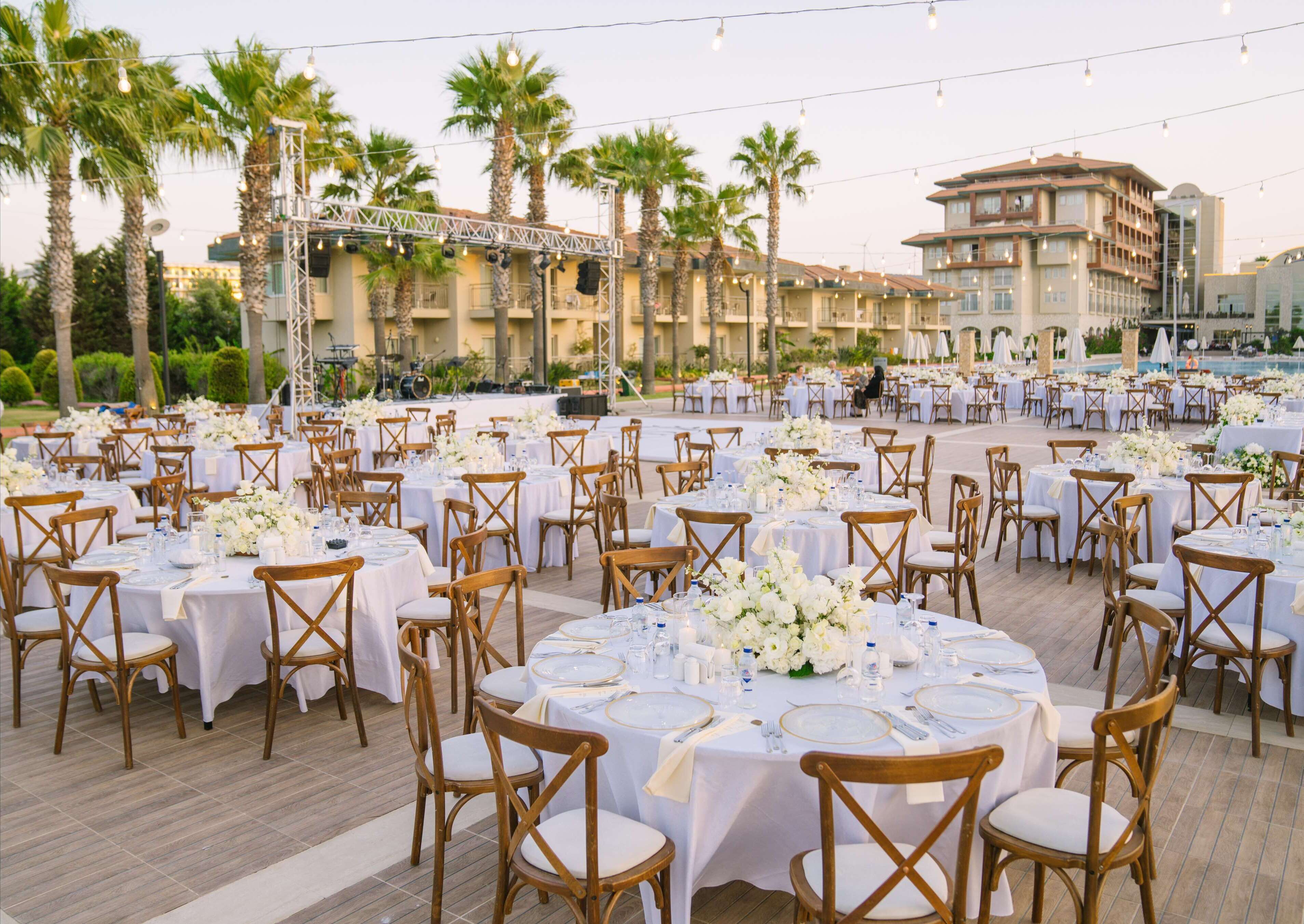 Un décor de banquet en plein air avec des tables rondes, des nappes blanches et des chaises en bois.
