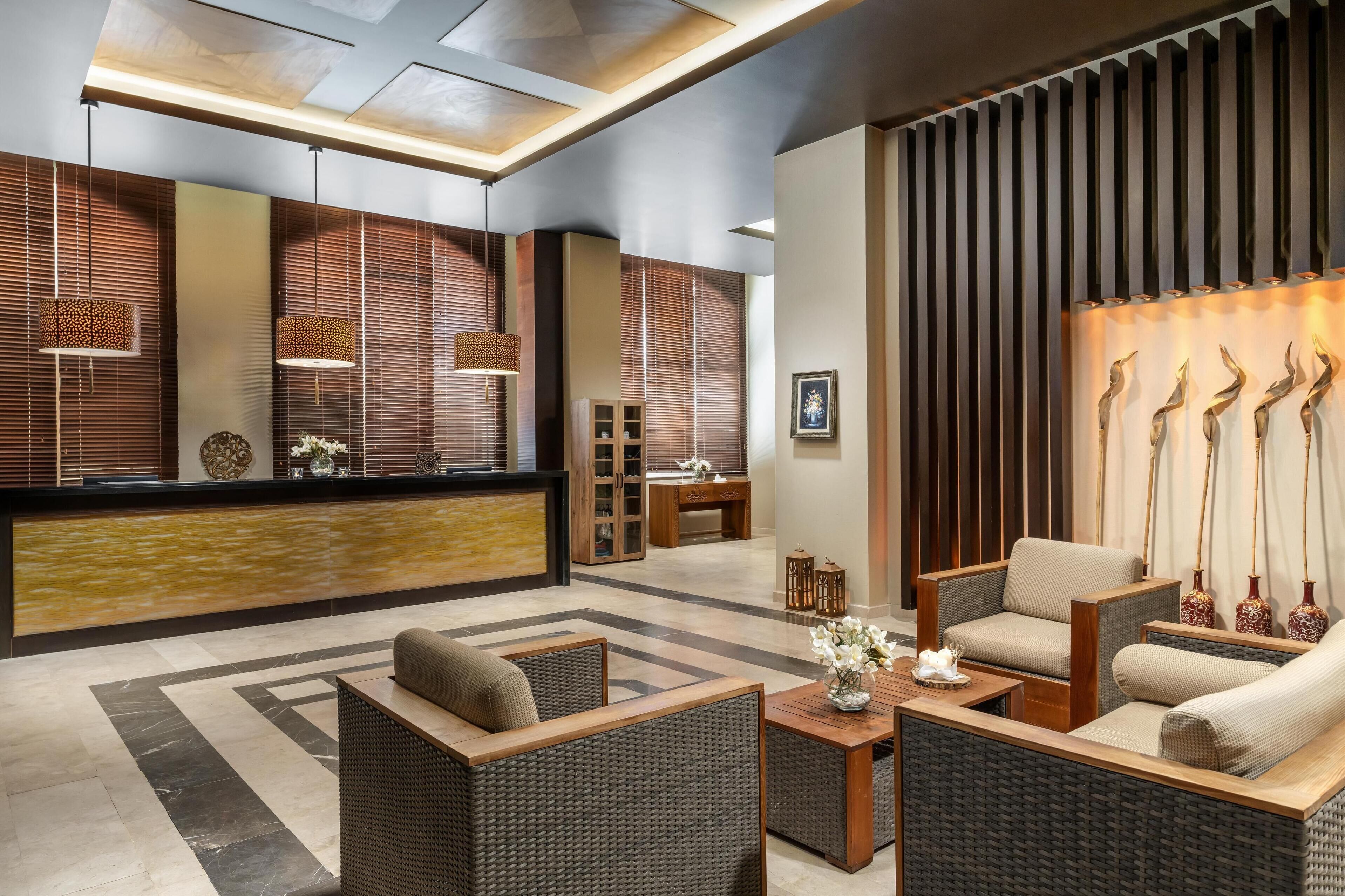 A modern lobby with wicker furniture, a reception desk, and decorative wall panels.