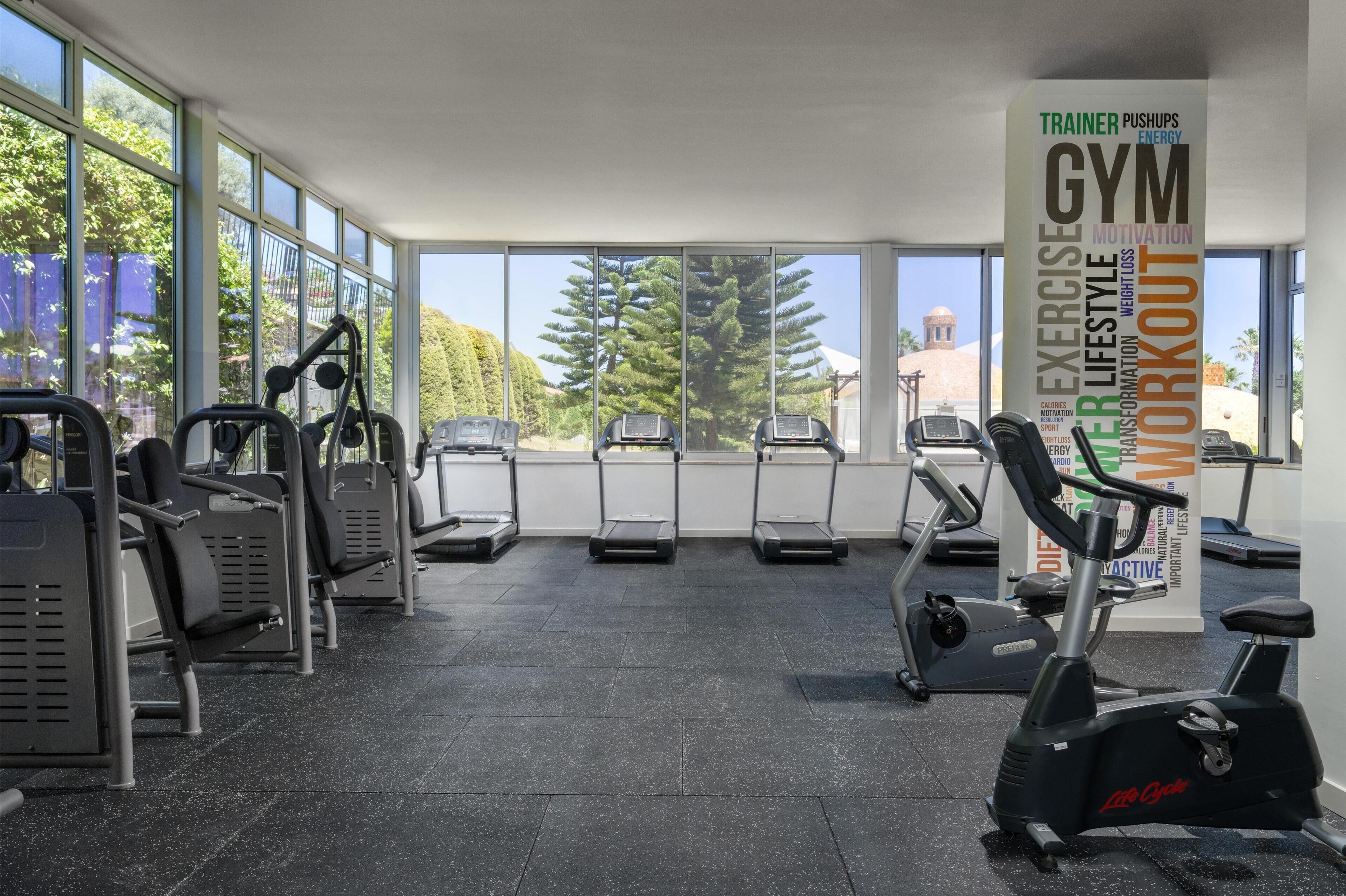A gym with various exercise equipment, large windows, and a motivational poster.
