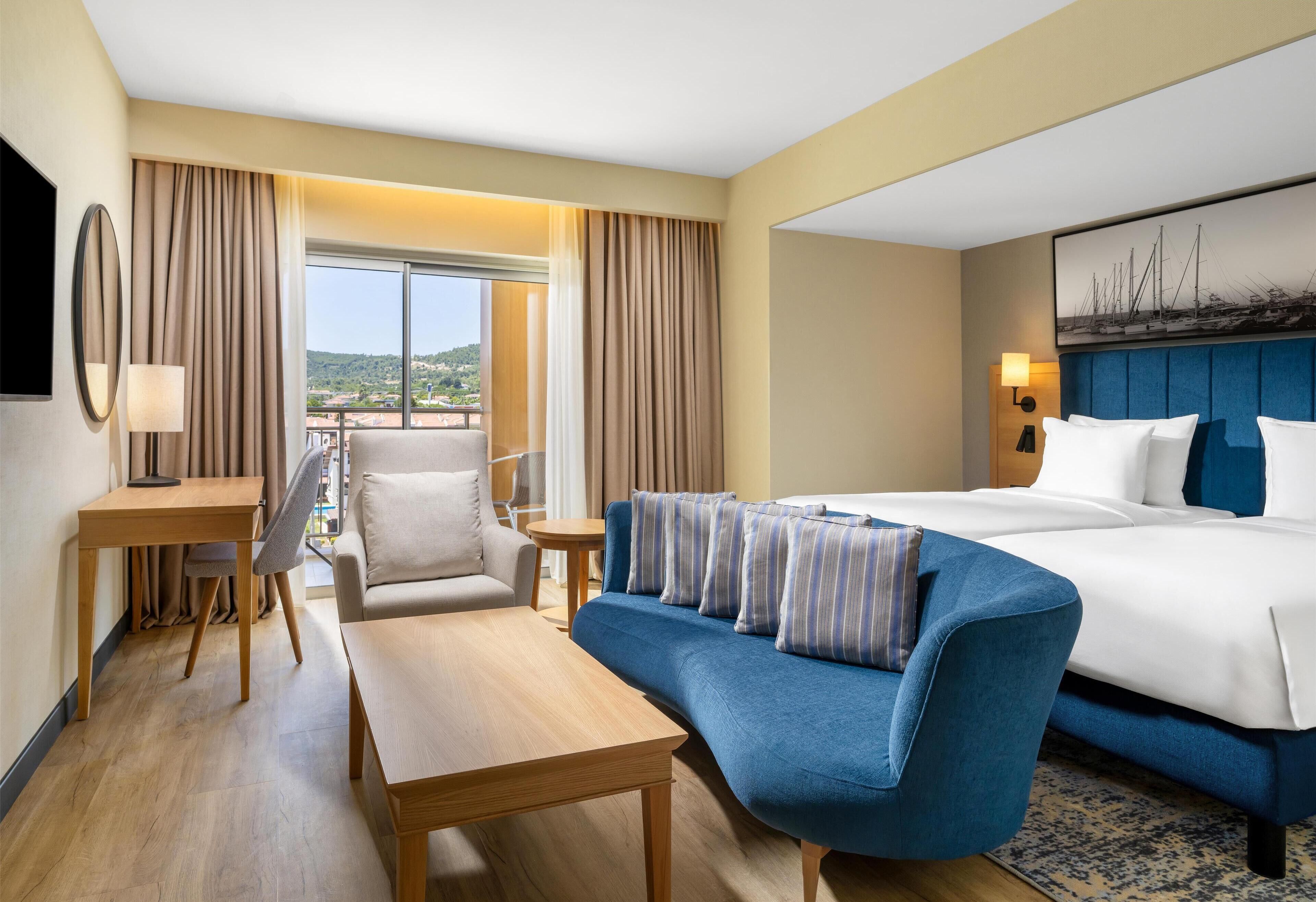 Een hotelkamer met een bed, een bank, een bureau, een stoel en uitzicht op de omgeving.