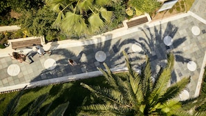 Vue aérienne d’un espace aménagé comprenant un chemin pavé, des bancs et des palmiers.