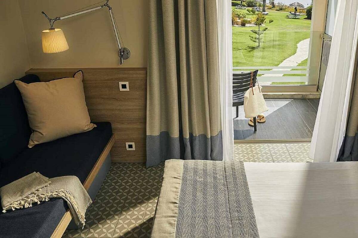 Habitación de hotel con cama, sofá, escritorio y vista a un campo de golf.