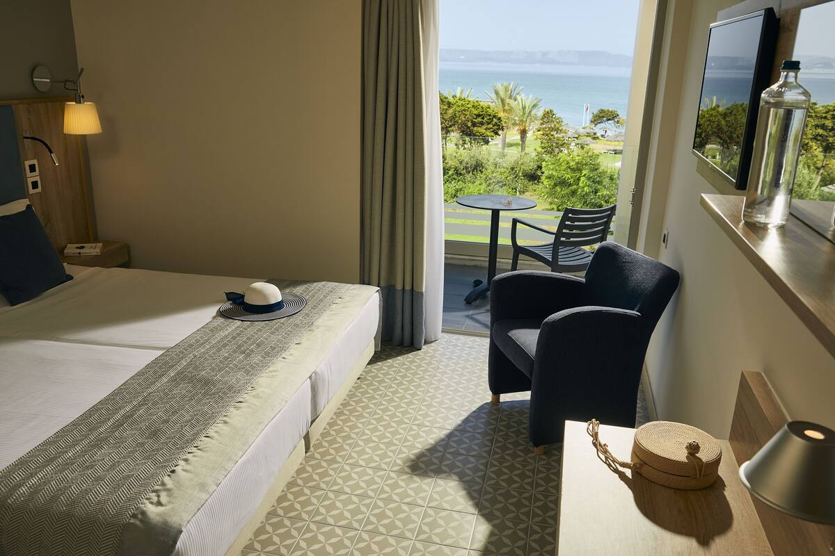 Habitación de hotel con cama, una silla, una mesita, una botella y vistas al mar.