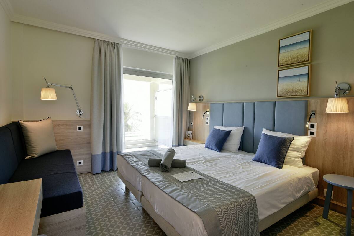 Habitación de hotel con una cama grande, un sofá, una mesita y vistas al exterior.