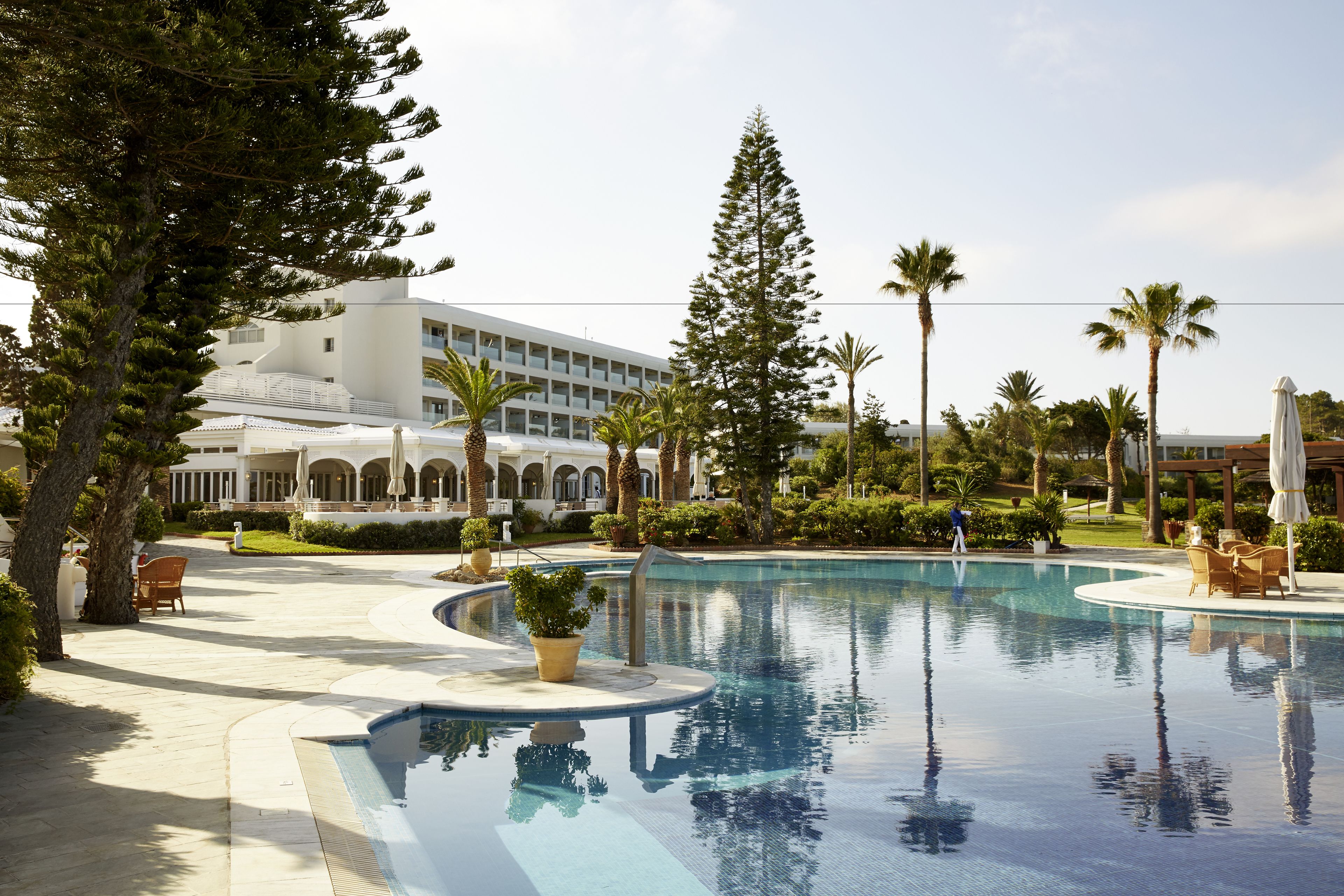 A swimming pool with a curved edge, surrounded by palm trees and a building with a modern design.