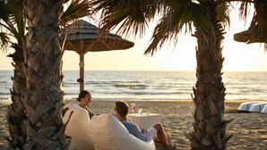 Two people relaxing on beach chairs under palm trees with a beach umbrella, overlooking the ocean. - ROBINSON KYLLINI BEACH (Andravida-Kyllini)