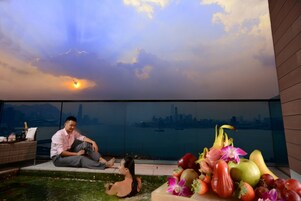 Un hombre y una mujer sentados junto a una piscina con vista a un paisaje urbano.