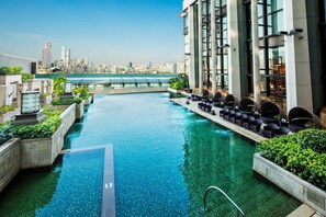 Una piscina infinita en la azotea con vistas a un horizonte urbano, rodeada de sillones de descanso y vegetación.